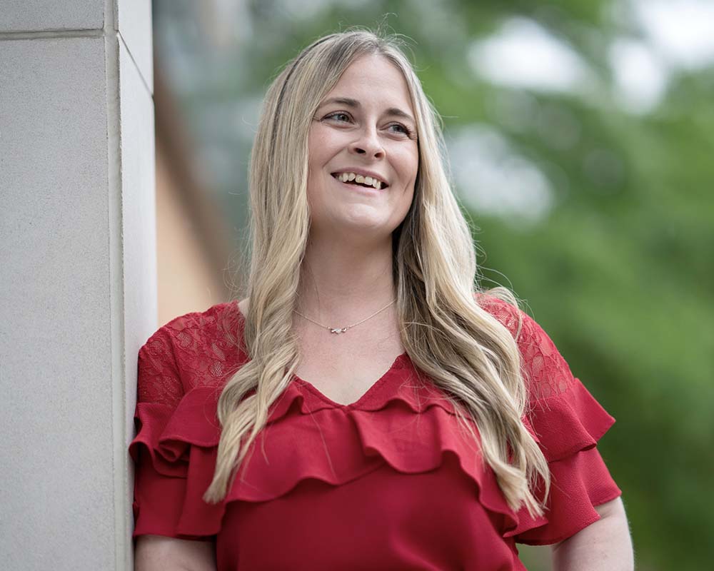 A UMGC graduate in professional clothing smiling in an outdoor location.