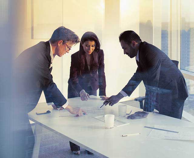 Two men and one woman in business attire standing around a table and looking at a document